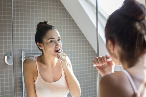 Medio volwassen vrouw tanden poetsen in de badkamer spiegel.